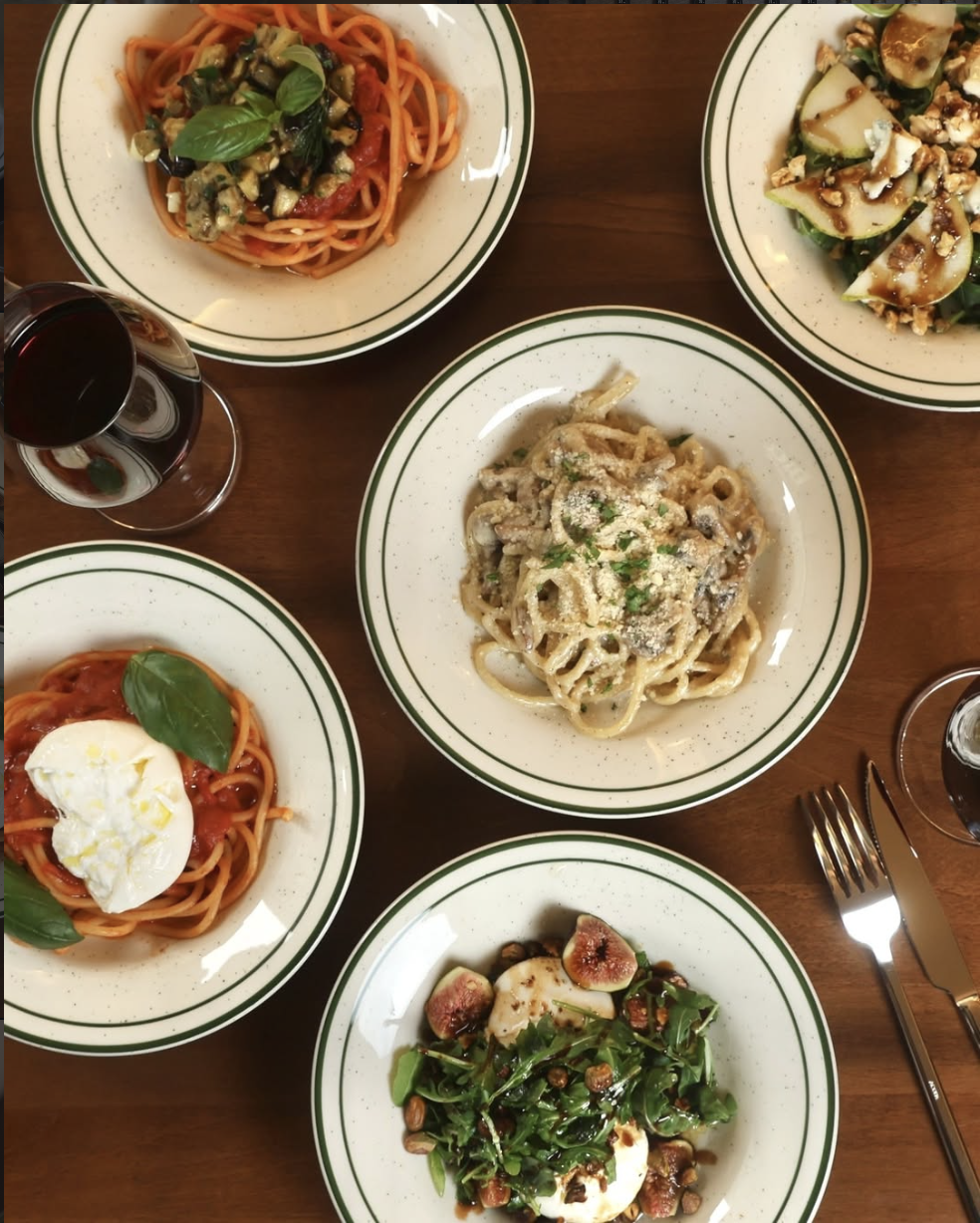 A full table of Bicchiere pasta, salads, and red wine